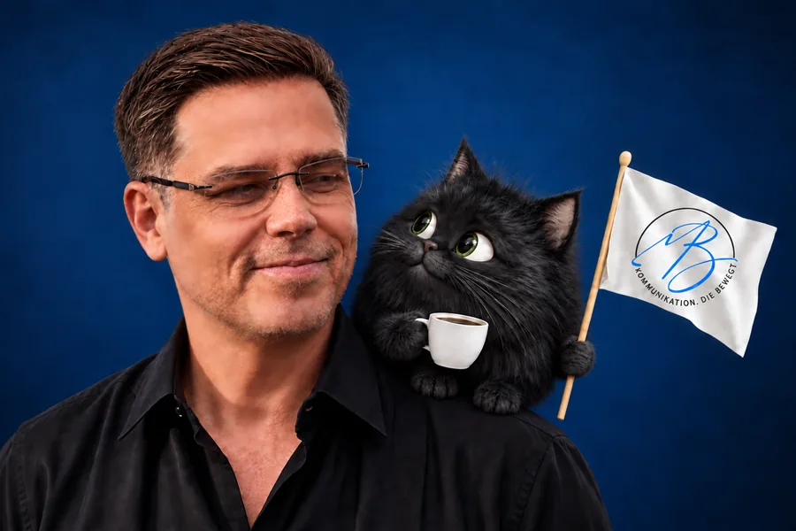 Mark Bottke mit einer schwarzen Katze auf der Schulter, die eine Tasse Kaffee und eine kleine Fahne mit dem Logo von MB-Trainings hält